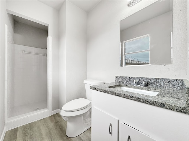 bathroom featuring hardwood / wood-style flooring, vanity, a tile shower, and toilet