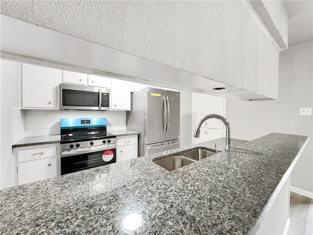 kitchen featuring appliances with stainless steel finishes, sink, dark stone countertops, white cabinets, and decorative backsplash