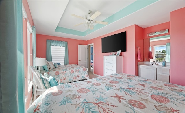 bedroom featuring a tray ceiling, a sink, and a ceiling fan