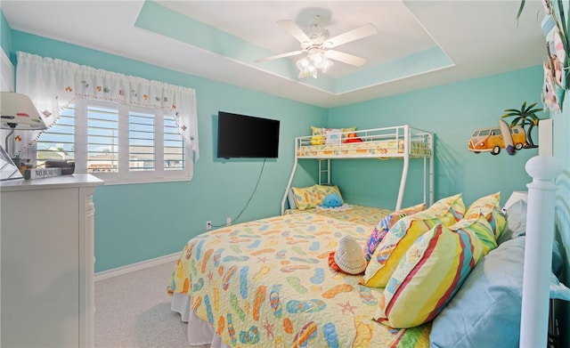 carpeted bedroom with a tray ceiling, ceiling fan, and baseboards