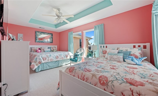 bedroom with ceiling fan, a tray ceiling, and carpet flooring