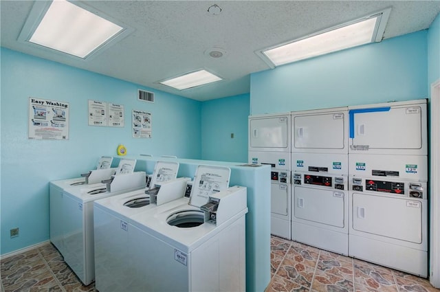 community laundry room featuring stacked washer and dryer, stone finish floor, washing machine and clothes dryer, and visible vents