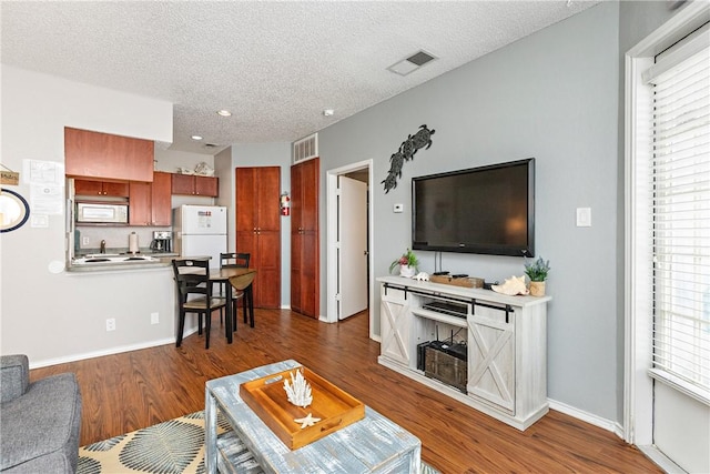 living area with a textured ceiling, wood finished floors, visible vents, and baseboards