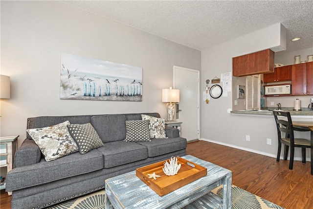 living area featuring a textured ceiling, dark wood finished floors, and baseboards