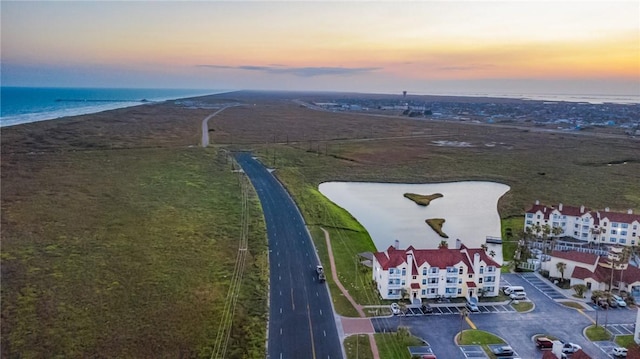 aerial view at dusk with a water view and a beach view