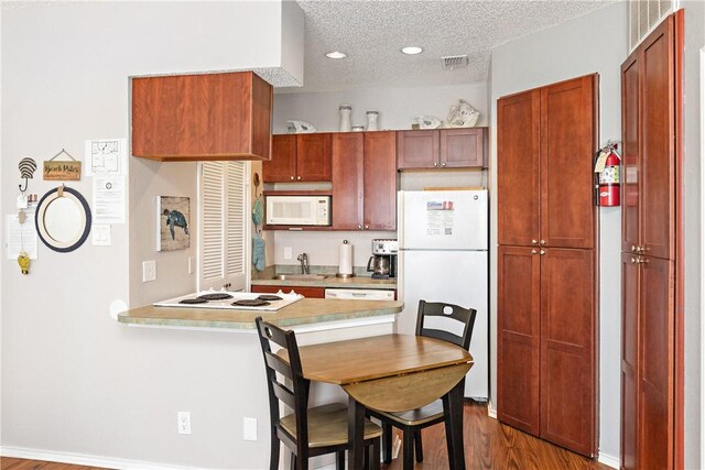 kitchen featuring white appliances, dark wood finished floors, a peninsula, light countertops, and a textured ceiling