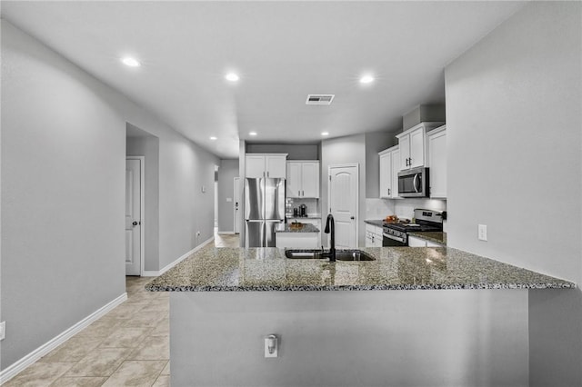 kitchen with kitchen peninsula, stainless steel appliances, sink, dark stone countertops, and white cabinets