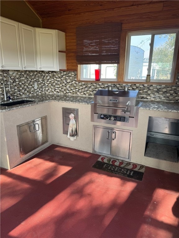 kitchen with a wealth of natural light, sink, light stone counters, and vaulted ceiling