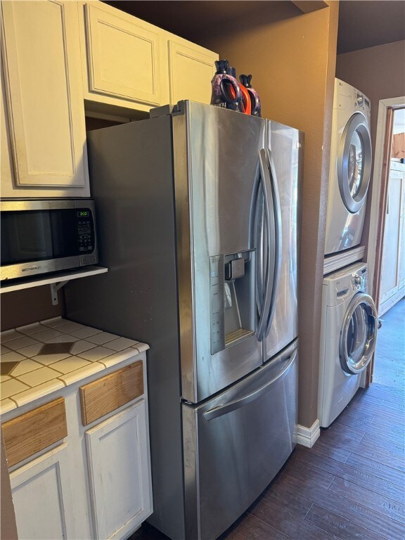 kitchen with tile counters, white cabinets, stacked washer / drying machine, and appliances with stainless steel finishes