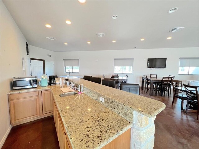 kitchen featuring light stone countertops, a healthy amount of sunlight, a spacious island, sink, and light brown cabinets