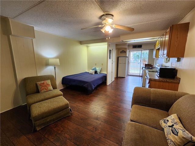 bedroom with access to outside, a textured ceiling, dark hardwood / wood-style floors, white fridge, and ceiling fan