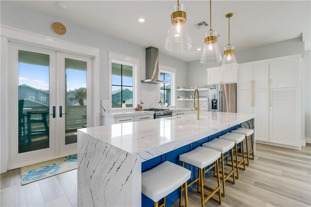 969 Banyan Beach Dr, Port Aransas, TX 78373 - kitchen featuring stainless steel appliances, wall chimney exhaust hood, white cabinets, french doors, and light stone counters
