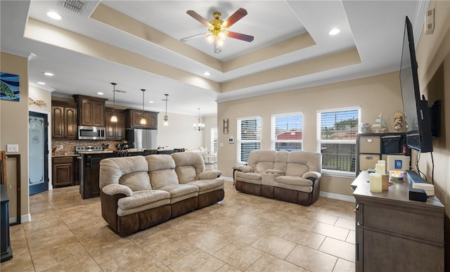 living room with crown molding, ceiling fan with notable chandelier, light tile patterned flooring, and a raised ceiling