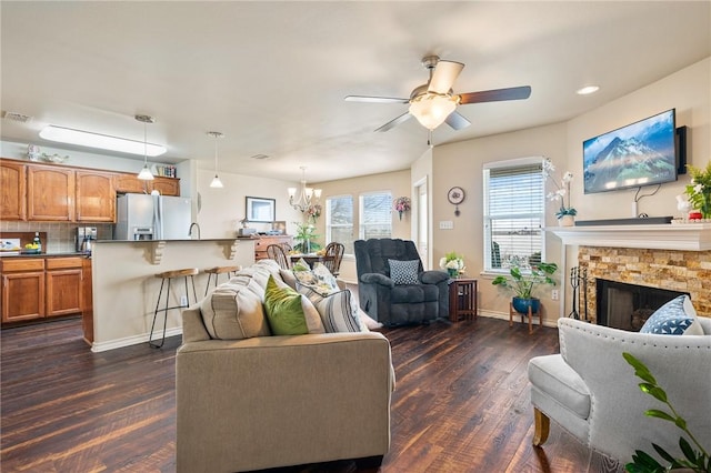 living room featuring ceiling fan with notable chandelier, a fireplace, visible vents, baseboards, and dark wood-style floors