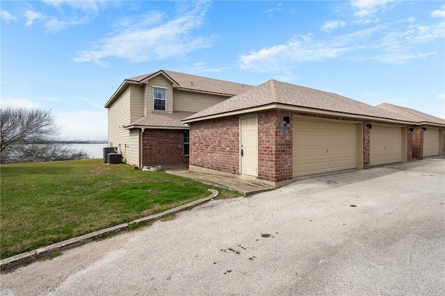 view of front facade featuring roof with shingles, an attached garage, cooling unit, a front yard, and brick siding