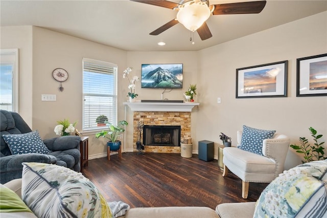 living area with ceiling fan, a stone fireplace, baseboards, and wood finished floors