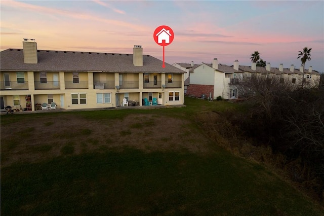 back of property at dusk with a balcony, a patio area, a chimney, and a lawn