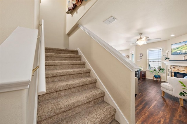 stairs featuring ceiling fan, hardwood / wood-style flooring, a fireplace, visible vents, and baseboards