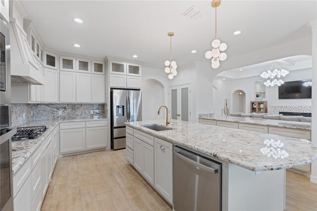 kitchen with appliances with stainless steel finishes, sink, white cabinets, hanging light fixtures, and an island with sink