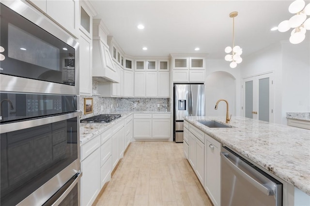 kitchen with pendant lighting, white cabinets, sink, light wood-type flooring, and stainless steel appliances