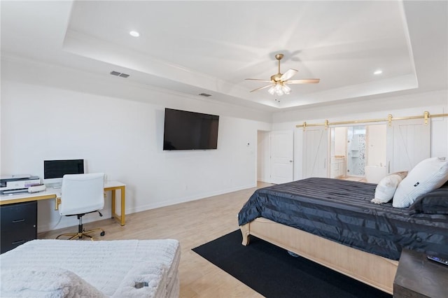 bedroom featuring a barn door, a tray ceiling, light hardwood / wood-style flooring, and ceiling fan