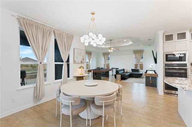 dining area with a raised ceiling, ceiling fan with notable chandelier, and light wood-type flooring