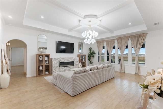 living room featuring a chandelier, a tiled fireplace, crown molding, and light hardwood / wood-style flooring