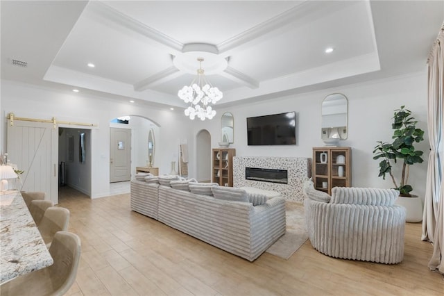 living room featuring crown molding, a barn door, a fireplace, a notable chandelier, and light hardwood / wood-style floors