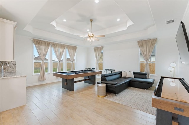 recreation room featuring ceiling fan, light hardwood / wood-style floors, pool table, and a tray ceiling