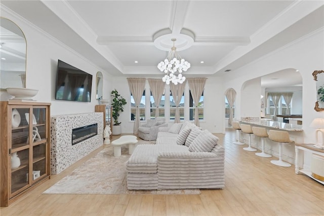 living room with light hardwood / wood-style floors, a tiled fireplace, ornamental molding, and a chandelier