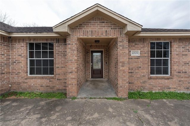 view of exterior entry featuring a shingled roof and brick siding