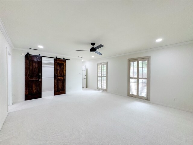 empty room featuring light colored carpet, ceiling fan, a barn door, and crown molding