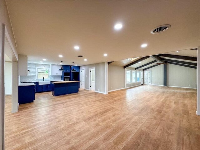 unfurnished living room featuring light hardwood / wood-style flooring, ceiling fan, lofted ceiling with beams, and sink