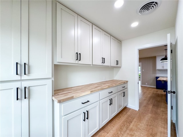 interior space with white cabinets, light wood-type flooring, butcher block countertops, and hanging light fixtures