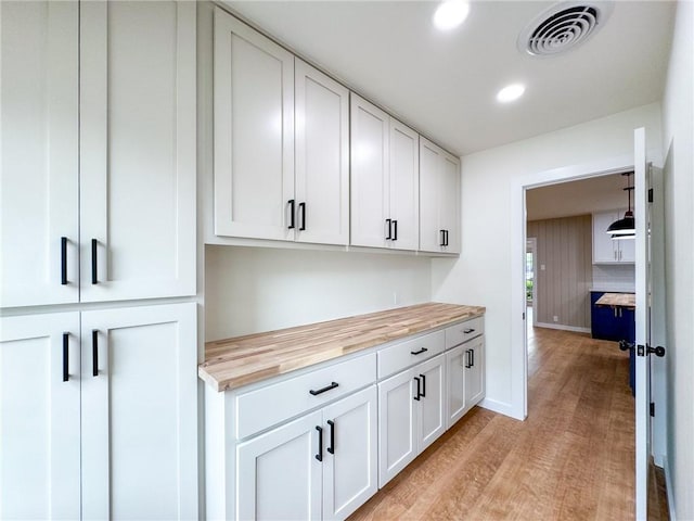 interior space with decorative light fixtures, butcher block countertops, light hardwood / wood-style floors, and white cabinetry