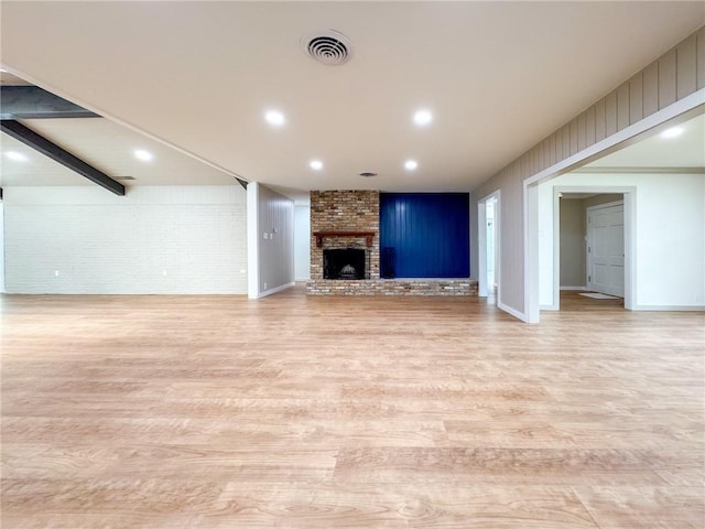 unfurnished living room featuring beam ceiling, light hardwood / wood-style flooring, a fireplace, and brick wall