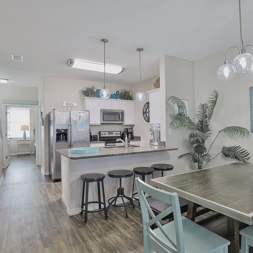 kitchen featuring white cabinetry, appliances with stainless steel finishes, dark hardwood / wood-style floors, hanging light fixtures, and kitchen peninsula