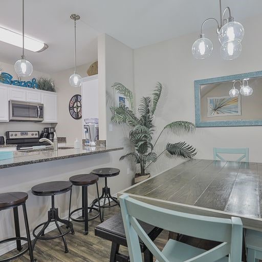 kitchen with stainless steel appliances, white cabinetry, decorative light fixtures, dark hardwood / wood-style floors, and a breakfast bar