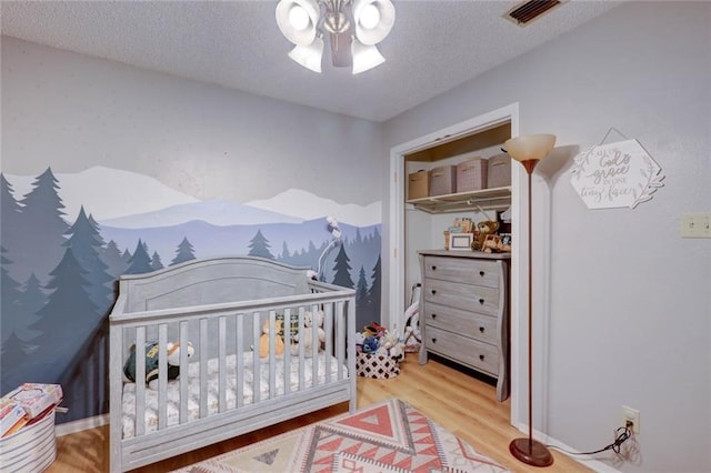 bedroom featuring a nursery area, hardwood / wood-style floors, ceiling fan, and a textured ceiling