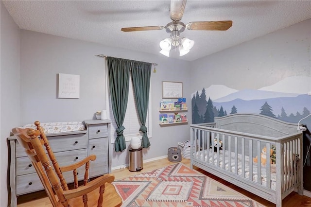 bedroom featuring a crib, light wood-type flooring, a textured ceiling, and ceiling fan