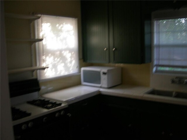 822 Indiana Ave, Corpus Christi, TX 78404 - kitchen with open shelves, tile counters, a sink, white microwave, and gas range oven