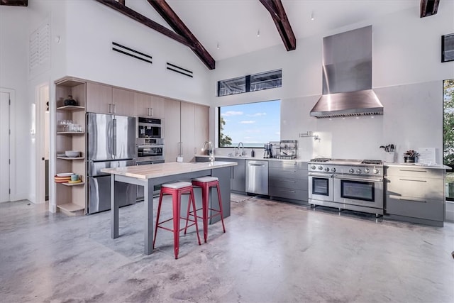 kitchen featuring appliances with stainless steel finishes, a kitchen breakfast bar, wall chimney exhaust hood, high vaulted ceiling, and beamed ceiling