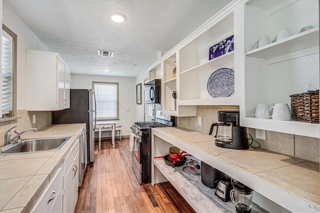 kitchen featuring tile counters, white cabinets, stainless steel appliances, and sink