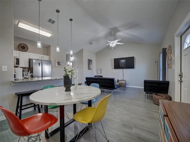 dining space with baseboards, visible vents, ceiling fan, wood finished floors, and vaulted ceiling