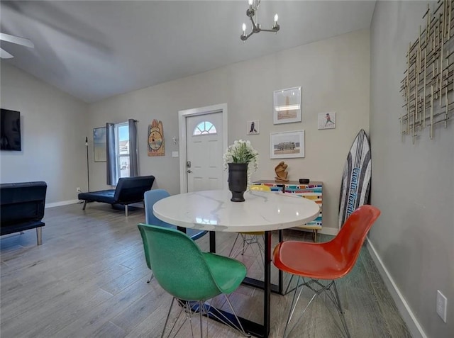 dining space featuring lofted ceiling, a notable chandelier, baseboards, and wood finished floors