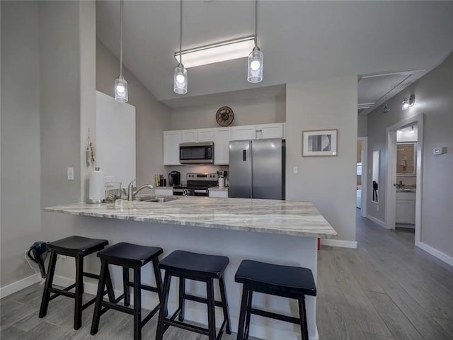 kitchen featuring stainless steel appliances, white cabinets, a sink, a peninsula, and a kitchen bar