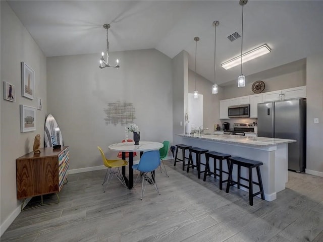 kitchen featuring visible vents, light wood-style flooring, appliances with stainless steel finishes, white cabinets, and a kitchen breakfast bar