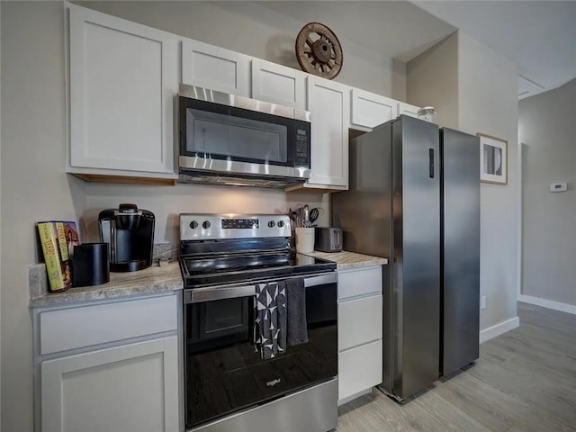 kitchen featuring light wood-type flooring, white cabinetry, appliances with stainless steel finishes, and baseboards