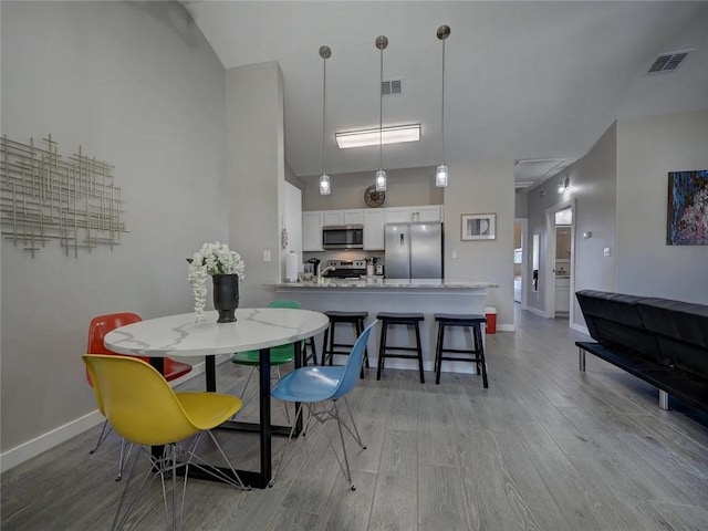 dining room featuring light wood-style flooring, visible vents, and baseboards