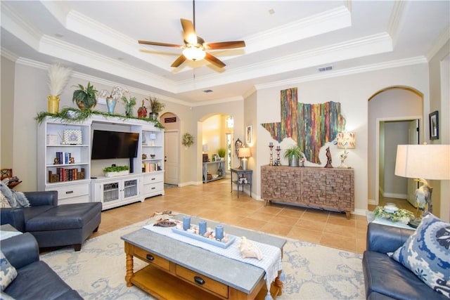 living area featuring arched walkways, a tray ceiling, a ceiling fan, light tile patterned flooring, and ornamental molding